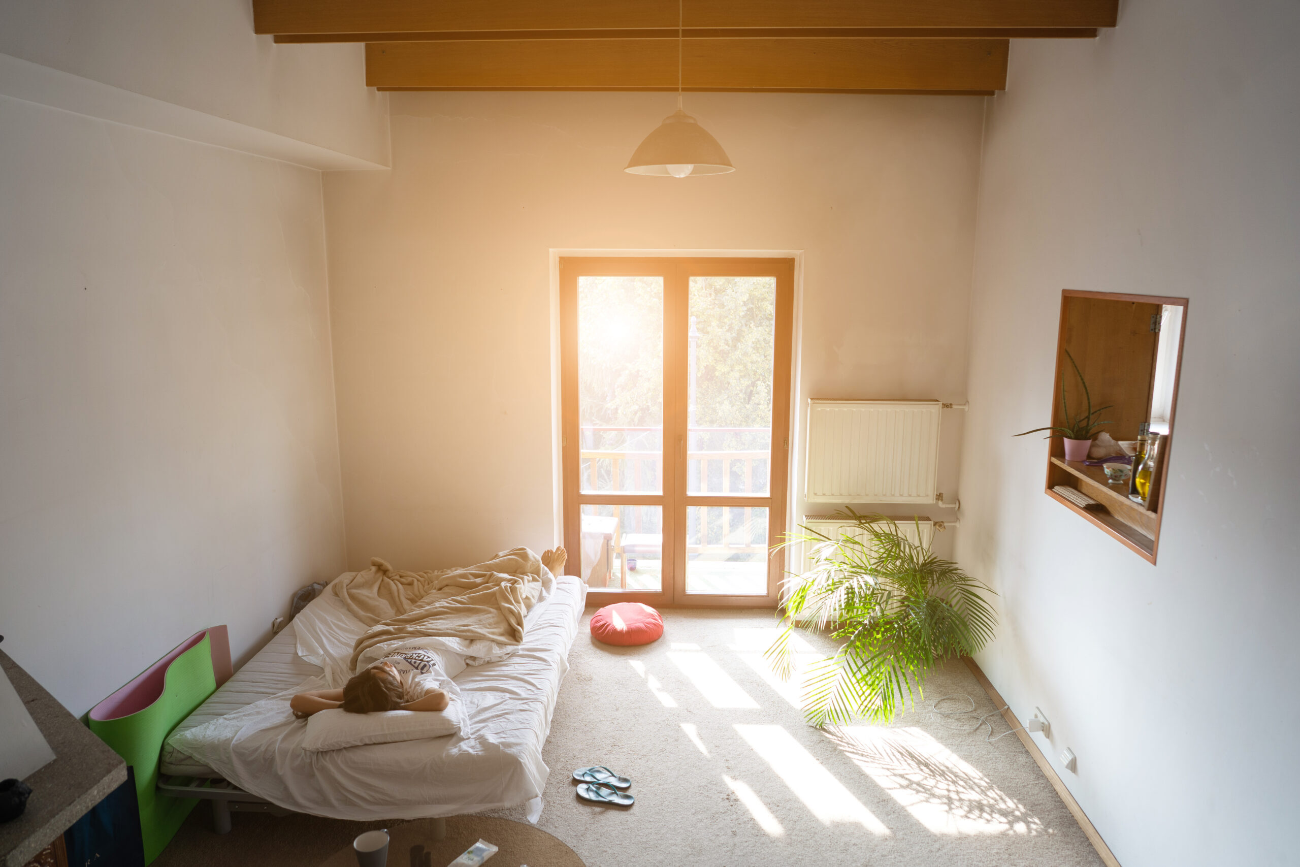 Beautiful young woman waking up in the morning. Girl looking outside through window