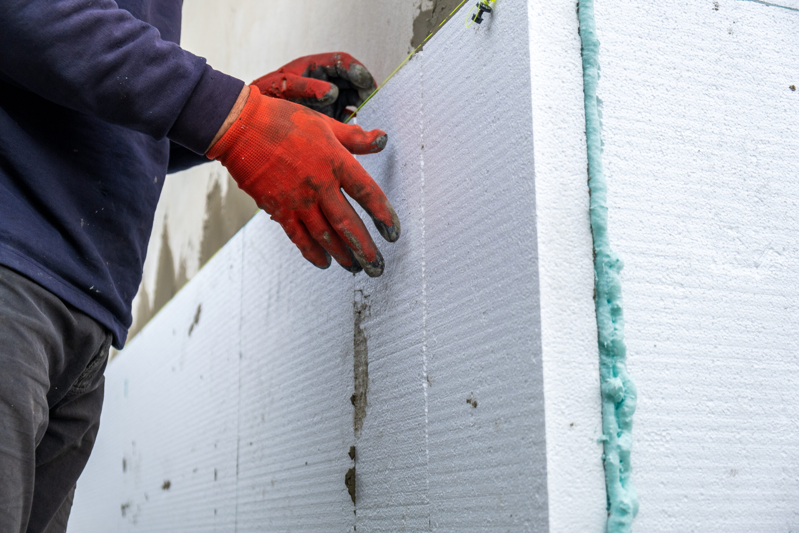 Construction worker installing styrofoam insulation sheets on house facade wall for thermal protection.